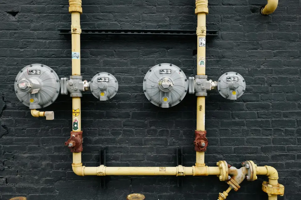 Gele gasleidingen met drukregelaars en afsluiters tegen een zwarte bakstenen muur