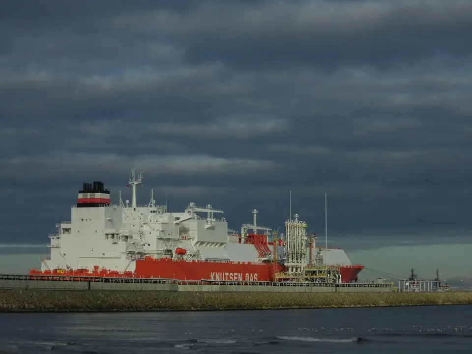 Een schip voor vloeibaar aardgas aan een kade onder een donkere wolkenlucht