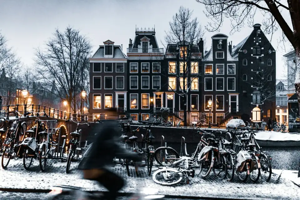 Grachtenpanden in Amsterdam op een winteravond, met besneeuwde fietsen langs de gracht en licht achter de ramen