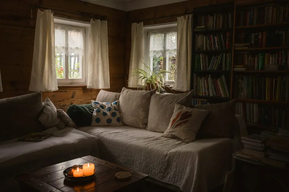 Een donkere woonkamer met een bank, boekenkasten en twee kaarsen op een houten tafel